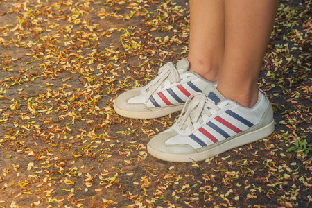 Woman wearing sneaker and standing on concrete floor surrounded with autumn leaves. (Autumn filter effect)の写真素材