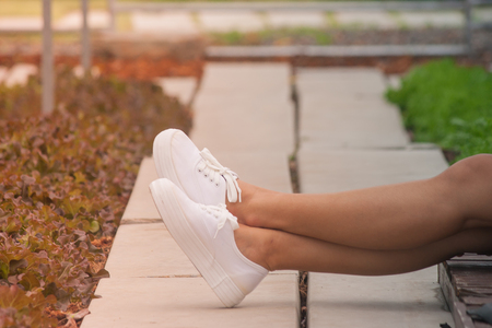 Close up woman's leg sitting on black pillow and wooden terrace in the garden with green natural background. (Autumn filter effect)の写真素材