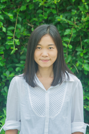 Asian woman portrait wear white shirt, smiling and looking forward with green tree background.の写真素材