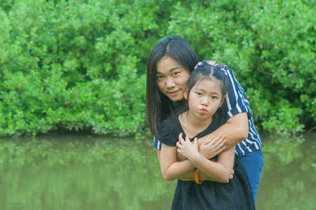 Adorable Family Concept : Asian woman and children standing on green grass, smiling and hug together at public park.の写真素材