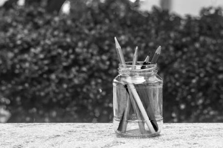 Various pencil in glass bottle on concrete floor with green bush background. (Black and White filter effect)の写真素材