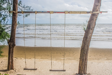 Wooden swing hanging from tree on the beach with seascape view background. (Vintage filter effect)の写真素材