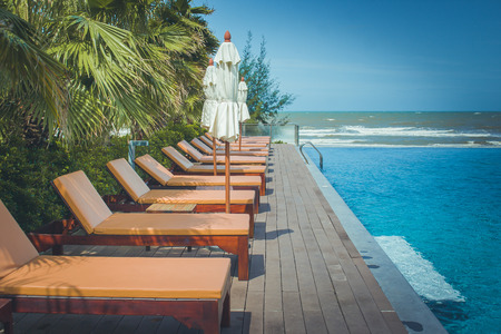 Vacation and Relaxation Concept : Daybed beside swimming pool in the resort with sea and blue sky background.の写真素材