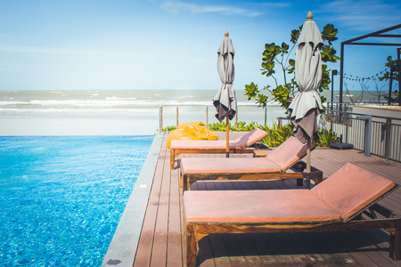 Vacation and Relaxation Concept : Daybed beside swimming pool in the resort with sea and blue sky background. (Vintage filter effect)の写真素材