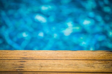 Close up wooden long chair with blue water in swimming pool background. (Selective Focus)の写真素材