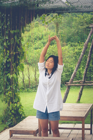 Relaxation Concept : Asian woman wear white shirt and stretch in the garden. (Vintage filter effect)の写真素材