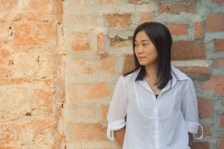 Shoot photo Asian woman portrait wear white shirt and looking sideways with red brick background (Vintage filter effect)の写真素材