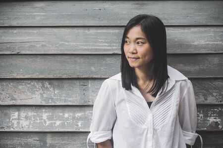 Shoot photo Asian woman portrait wear white shirt and looking sideways with wooden wall background (Vintage filter effect)の写真素材
