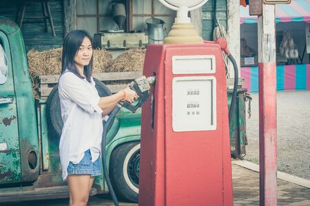 Portrait Asian woman holding red petrol pump nozzle with retro car background at countryside. (Vintage filter effect)の写真素材