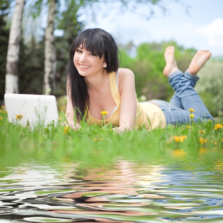 Cute woman with white laptop in the park with dandelions の写真素材
