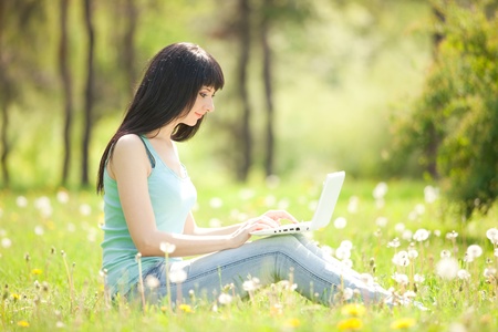 Cute woman with white laptop in the park with dandelionsの写真素材