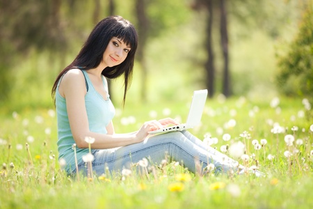 Cute woman with white laptop in the park with dandelionsの写真素材