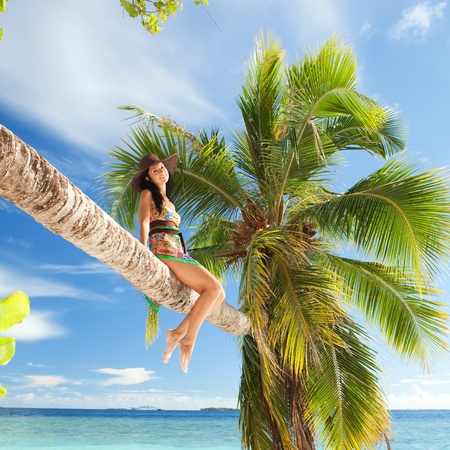 Fashion woman siting upon palm tree on the beachの写真素材