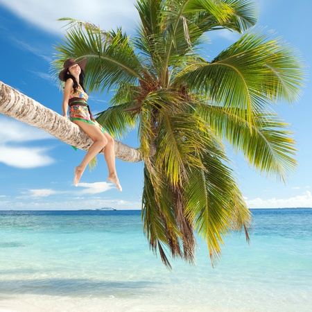 Fashion woman siting upon palm tree on the beachの写真素材
