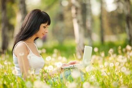 Cute woman with white laptop in the park with dandelionsの写真素材