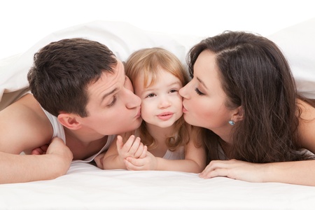 Happy family, mother, father and daughter on the white bedの写真素材