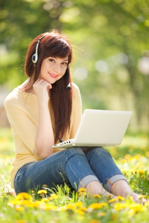 Cute woman in earphones with white laptop in the parkの写真素材