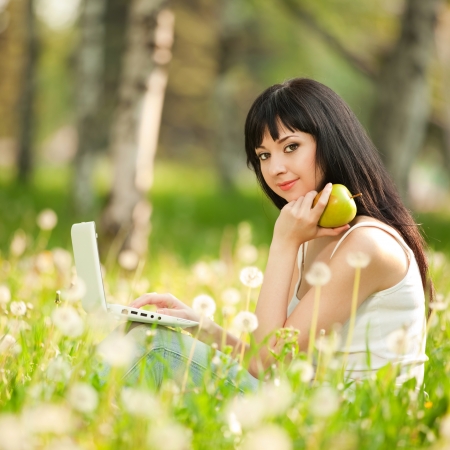 Cute woman with white laptop in the park with dandelionsの写真素材