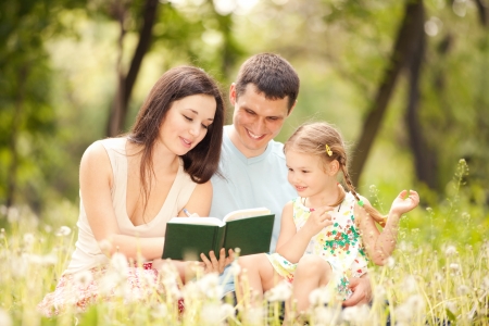 Happy mother, father and daughter read a book in the parkの写真素材