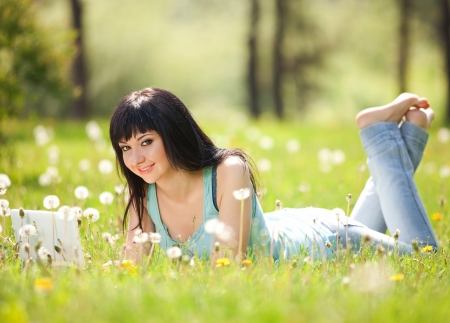 Cute woman with white laptop in the park with dandelionsの写真素材