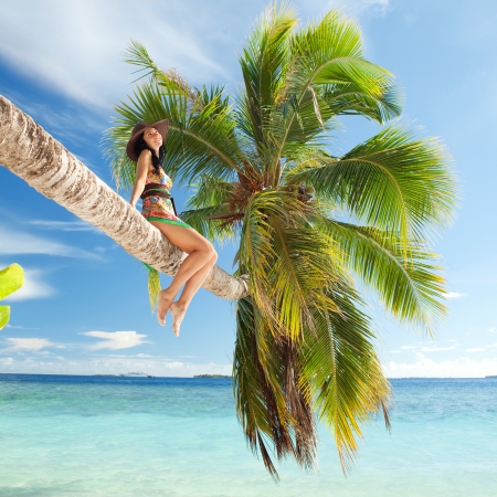 Fashion woman siting upon palm tree on the beachの写真素材