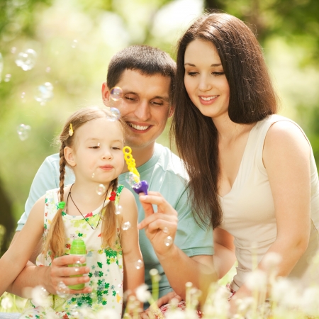 Happy mother, father and daughter blowing bubbles in the parkの写真素材