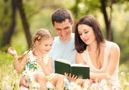 Happy mother, father and daughter read a book in the parkの写真素材