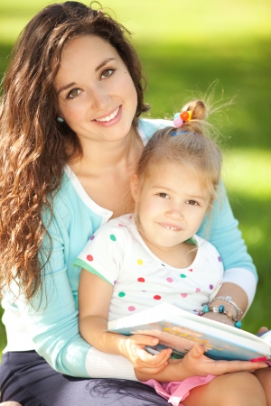 Mother with daughter reading a book in the parkの写真素材