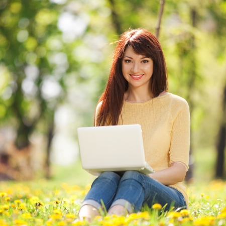 Cute woman with white laptop in the park with dandelionsの写真素材