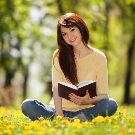 Young woman reading a book in the park with flowersの写真素材