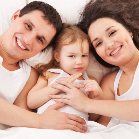 Happy family, mother, father and daughter resting on the white bedの写真素材