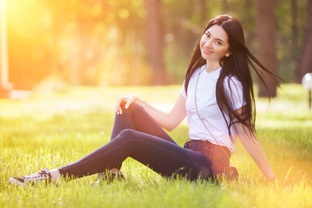 Young woman relax in the park on green grass. Beauty nature scene with colorful background, trees at summer season. Outdoor lifestyle. Happy smiling woman sitting on green grassの写真素材