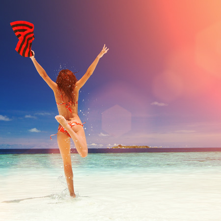 Happy young woman jumping on the beach. Happy lifestyle. White sand, blue sky, sun and crystal sea of tropical beach. Vacation at Paradise. Ocean beach relax, travel to islands. Sun lightの写真素材
