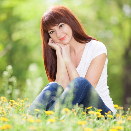 Young woman relax in the park with flowers. Beauty nature scene with colorful background, trees and flowers at summer season. Outdoor lifestyle. Happy smiling woman sitting on green grassの写真素材