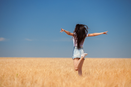 Happy woman enjoying the life in the field Nature beauty, blue sky and field with golden wheat. Outdoor lifestyle. Freedom concept. Woman jump in summer fieldの写真素材