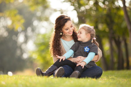 Mother and daughter walking in the autumn park. Beauty nature scene with colorful background, yellow trees and leaves at fall season. Autumn outdoor lifestyle. Happy family relax on green grassの写真素材
