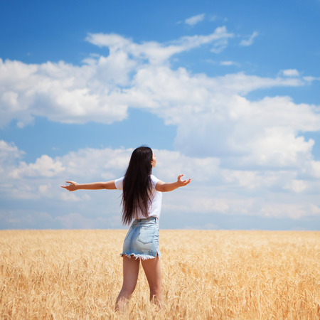 Happy woman enjoying the life in the field Nature beauty, blue cloudy sky and colorful field with golden wheat. Outdoor lifestyle. Freedom concept. Woman in summer fieldの写真素材