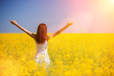 People freedom success concept. Happy woman in the field with flowers at sunny day in the countryside. Nature beauty background, blue sky and yellow flowers. Outdoor lifestyle.の写真素材