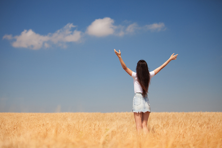 Happy woman enjoying the life in the field Nature beauty, blue cloudy sky and colorful field with golden wheat. Outdoor lifestyle. Freedom concept. Woman in summer fieldの写真素材