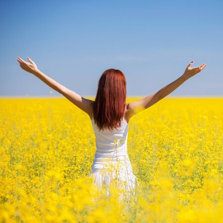 People freedom success concept. Happy woman in the field with flowers at sunny day in the countryside. Nature beauty background, blue sky and yellow flowers. Outdoor lifestyle.の写真素材