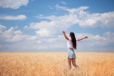 Happy woman enjoying the life in the field Nature beauty, blue sky and field with golden wheat. Outdoor lifestyle. Freedom concept. Woman jump in summer fieldの写真素材