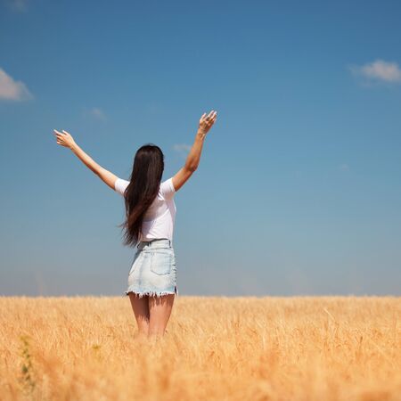 Happy woman enjoying the life in the field Nature beauty, blue sky and field with golden wheat. Outdoor lifestyle. Freedom concept. Woman jump in summer fieldの写真素材