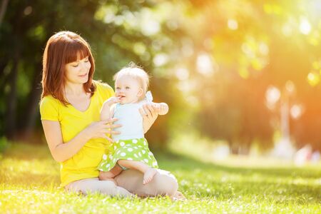 Happy mother and daughter in sunny summer park. Beauty nature scene with family outdoor lifestyle. Happy family resting together on the green grass, having fun outdoor. Happiness and harmony in family life.の写真素材