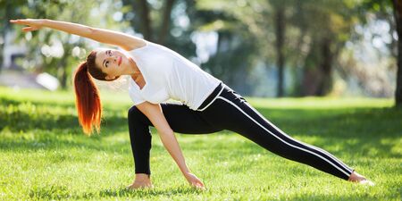 Yoga outdoor. Happy woman doing yoga exercises, stretching in the park. Yoga meditation in nature. Concept of healthy lifestyle and relaxation. Pretty woman practicing yoga on the grassの写真素材
