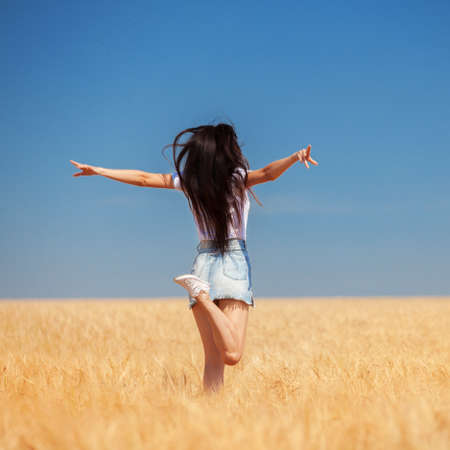 Happy woman enjoying the life in the field Nature beauty, blue sky and field with golden wheat. Outdoor lifestyle. Freedom concept. Woman jump in summer fieldの写真素材