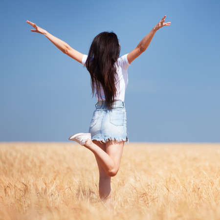 Happy woman enjoying the life in the field Nature beauty, blue sky and field with golden wheat. Outdoor lifestyle. Freedom concept. Woman jump in summer fieldの写真素材