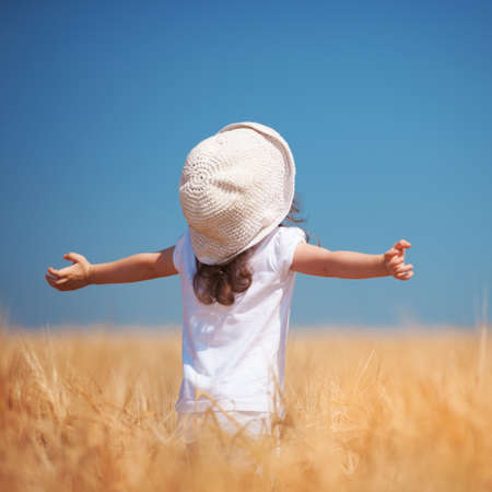 Happy girl walking in golden wheat, enjoying the life in the field. Nature beauty, blue sky and field of wheat. Family outdoor lifestyle. Freedom concept. Cute little girl in summer fieldの写真素材