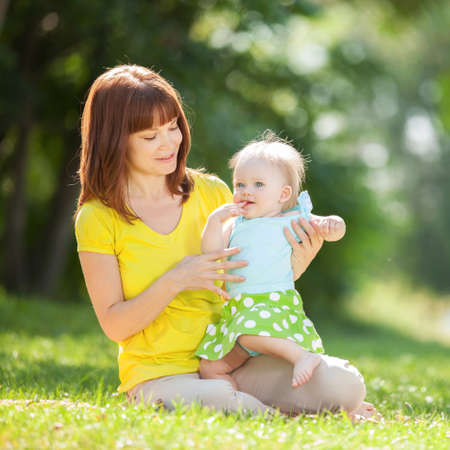 Happy mother and daughter in the summer park. Beauty nature scene with family outdoor lifestyle. Happy family resting together on the green grass, having fun outdoor. Happiness and harmony in family life.の写真素材
