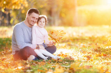 Happy father and daughter in the autumn park. Beauty nature scene with family outdoor lifestyle. Happy family resting together on green grass, having fun outdoor. Happiness and harmony in family lifeの写真素材