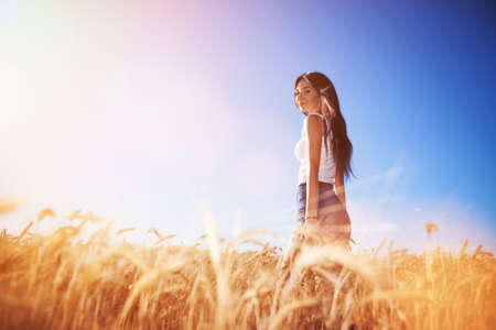 Happy woman enjoy the life in the field. Nature beauty, blue sky,white clouds and field with golden wheat. Outdoor lifestyle. Freedom concept. Woman walk in summer fieldの写真素材